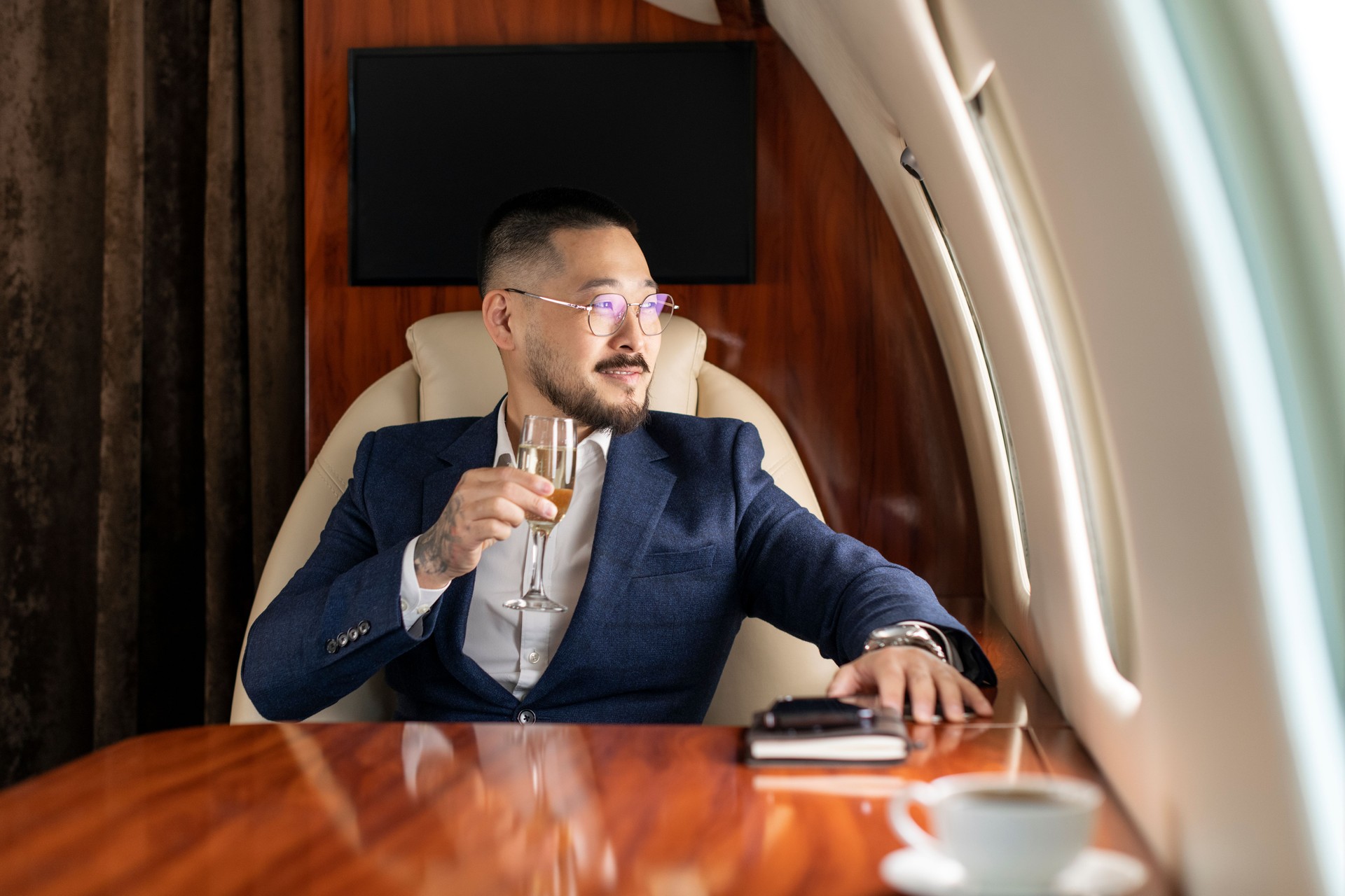 Asian businessman in suit and glasses sits in private jet and drinks champagne, Korean financier manager